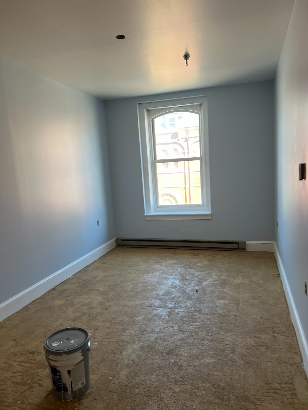 Pale blue bedroom with white trim and an arched window after interior painting