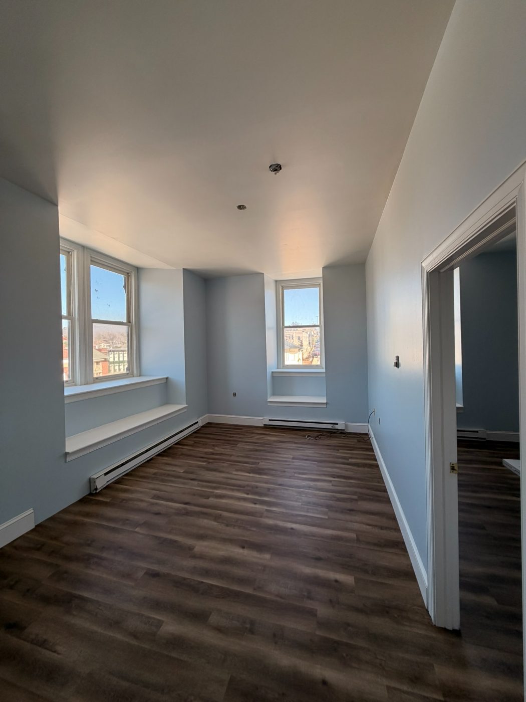 Soft blue bedroom with white window casings and refinished hardwood floors