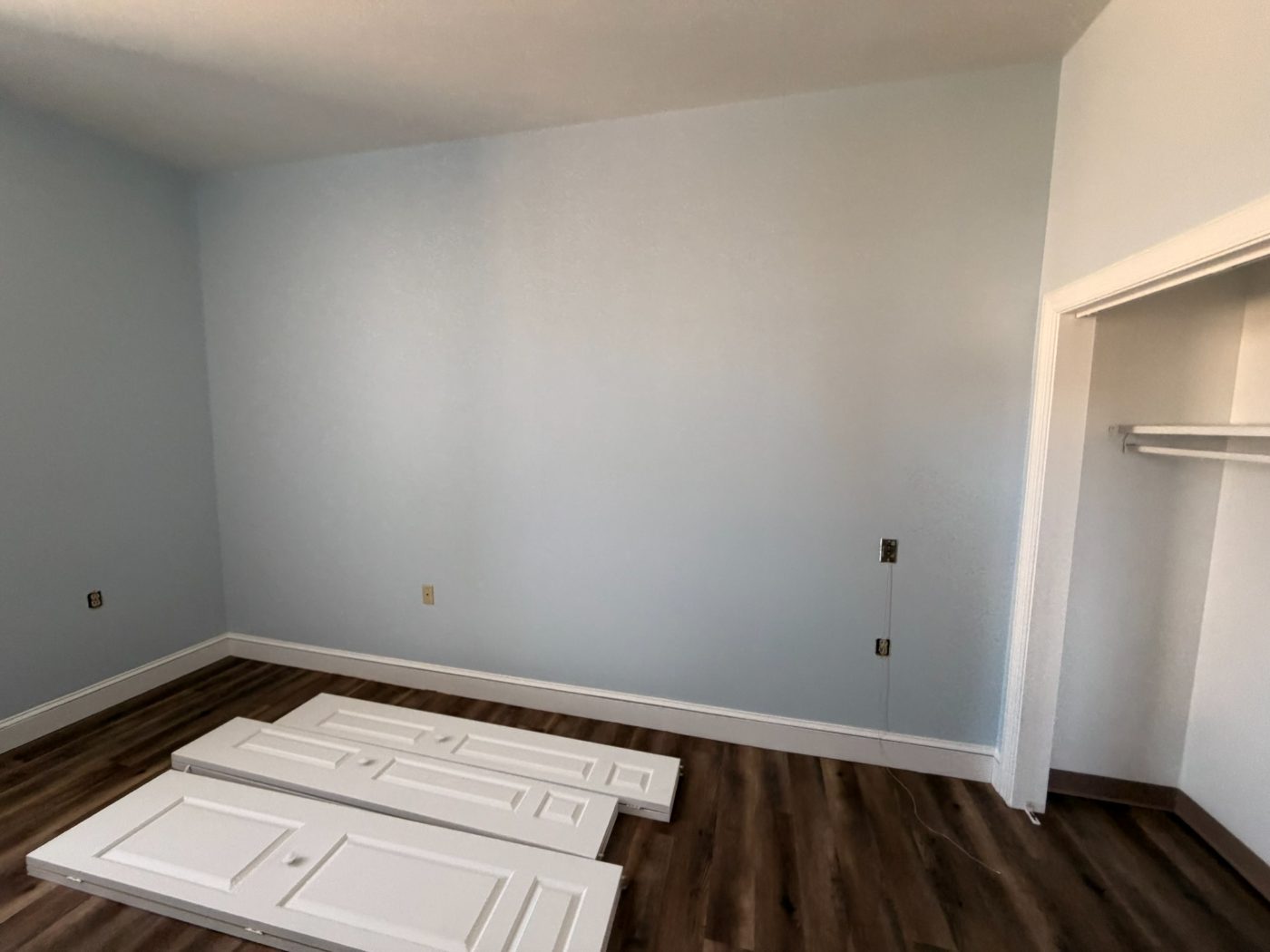 Spacious light blue bedroom with white trim and wood-look flooring