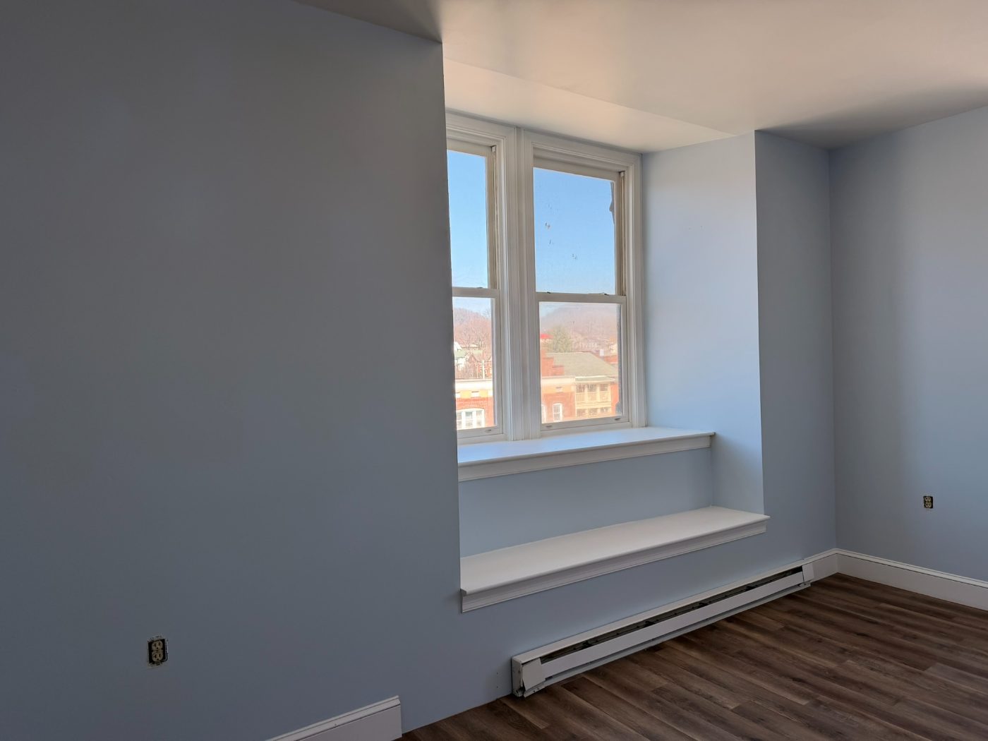 Blue bedroom with white window seat and hardwood floor overlooking State College